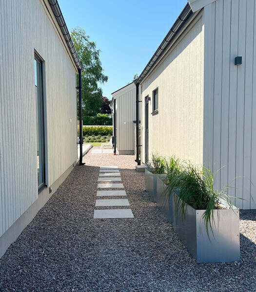 Foto på stegstenar i grus samt planteringslådor från Wernamo design innehållandes tuvrör. Trädgårdsdesign.